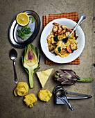 Pappardelle with artichokes and prawns surrounded by ingredients