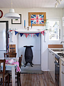 Landhausküche mit Eisenofen in stillgelegtem Kamin, darüber DIY-Wimpelkette und England-Fahne in Bilderrahmen