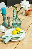 Lemons on stacked plates, peony in demijohn and vintage candlesticks on wooden table