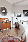 Old chest of drawers below sunburst mirror in bedroom