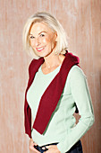 An older blonde woman wearing a light green knitted jumper with a dark red jumper over her shoulders