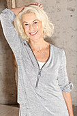 An older blonde woman wearing a light grey, long-sleeved top with a zip