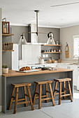 Counter with wooden barstools in open-plan renovated kitchen with grey wall