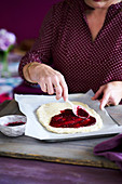 Spreading a raw shortcrust pastry base with raspberry jam