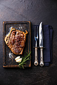 Gegrilltes Barbecue-Steak mit Messer und Gabel auf dunklem Untergrund
