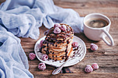 Stack of banana pancakes topped with chocolate drizzle and frozen raspberries