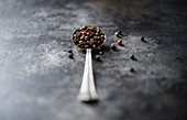 A vintage spoon filled with beautiful tri-color peppercorn on a dark rustic surface