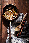 Old world copper pot filled with asian noodle soup and mushrooms on rich wood surface