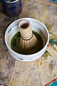 Water and matcha tea powder being mixed with a tea whisk