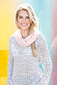 A young blonde woman wearing a knitted jumper and a pink loop scarf