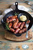 Bacon-wrapped chipolata sausages with mustard in a pan