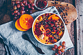 Smoothie Bowl mit Kaki, Papaya, Granatapfelkernen, Trauben, Kakaonibs, Himbeerkompott, Granola und Physalis