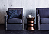 Kupferfarbener Beistelltisch zwischen blauen Sesseln mit Polsternägeln