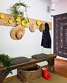 Rustikale Holzbank, Korb und Gummistiefel, darüber Holz-Garderobe mit Hüten