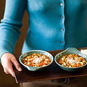 A woman serving two bowls of minestrone soup
