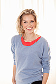 A young blonde woman wearing a blue jumper over a red top