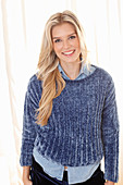 Junge blonde Frau in Jeanshemd und blauem Pullover