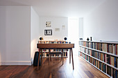 Desk in front of narrow, floor-to-ceiling window and next to long, low bookcase