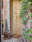 Outside shower with wooden wall next to climber-covered brick wall