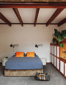 Bed linen with zigzag pattern in bedroom with wooden ceiling beams