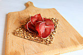 A slice of bresaola on a cracker on a wooden board (Veltlin, Lombardy, Italy)