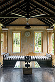 Sri Lanke mask on glass-topped table, striped bed in garden pavilion