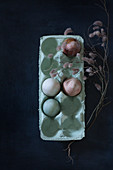 Dried flowers around painted eggs in egg box