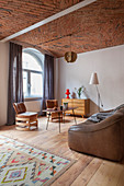 Leather sofa and designer leather chairs in open-plan interior with brick ceiling