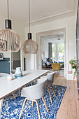 Pendant lamps above dining table and shell chairs with view into living room through open double doors