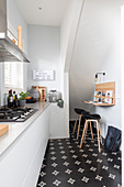 weiße Einbauküche und kleine Frühstückstheke mit Barhockern unter Treppenwand