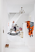 Kind auf Schaukelpferd in weißem Treppenhaus