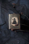 Tea caddy with silhouette ornamentation under tulle on crumpled black fabric