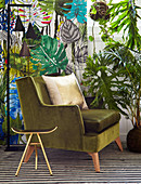 Gilt stool and green velvet armchair in front of leaf-patterned wallpaper