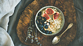Healthy winter breakfast: Rice coconut porridge with figs, berries and hazelnuts in bowl over rustic wooden board