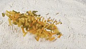 Dry pasta falling into flour, slow motion
