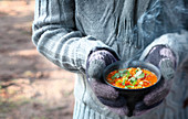 Gloved hands holding a bowl of warm soup from the grill