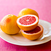 Rosa Grapefruits, ganz und halbiert, auf Teller