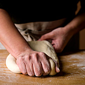 Baker kneading dough on a butcher block wood surface