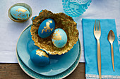 Ostereier und selbstgebastelte Pappmache-Schalen in Blau und Gold