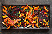 Colourful oven-roasted vegetables with peppered chicken on a baking tray
