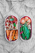 Bentobox mit Tomaten-Nudeln und Ofen-Süsskartoffeln und mit Melonenkugeln und Avocado