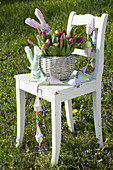 Korb mit Tulpenstrauß, DIY-Stoffhasen und Girlande auf Stuhl im Garten