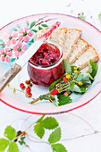 A jar of wild strawberry jam and slice of bread on an old enamel plate