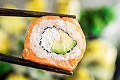 Chopsticks hold philadelphia roll over blurred plate of sushi