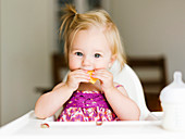 A little girl eating in a high chair