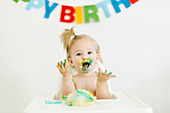 A little girl sitting in a high chair and eating a muffin for her first birthday