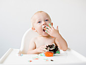 A little boy sitting in a high chair and eating a muffin for his first birthday