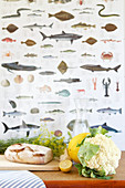 Bread, cauliflower, dill, melon, lemon and a water carafe in front of fish wallpaper