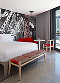 Modernes Hotelzimmer mit Doppelbett und Sitzecke, schwarz-weiße Tapete an der Wand