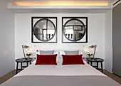Two round mirrors in square frames above bed with red pillows